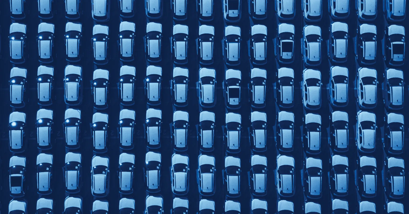 Rows of identical new cars parked in a grid, seen from above