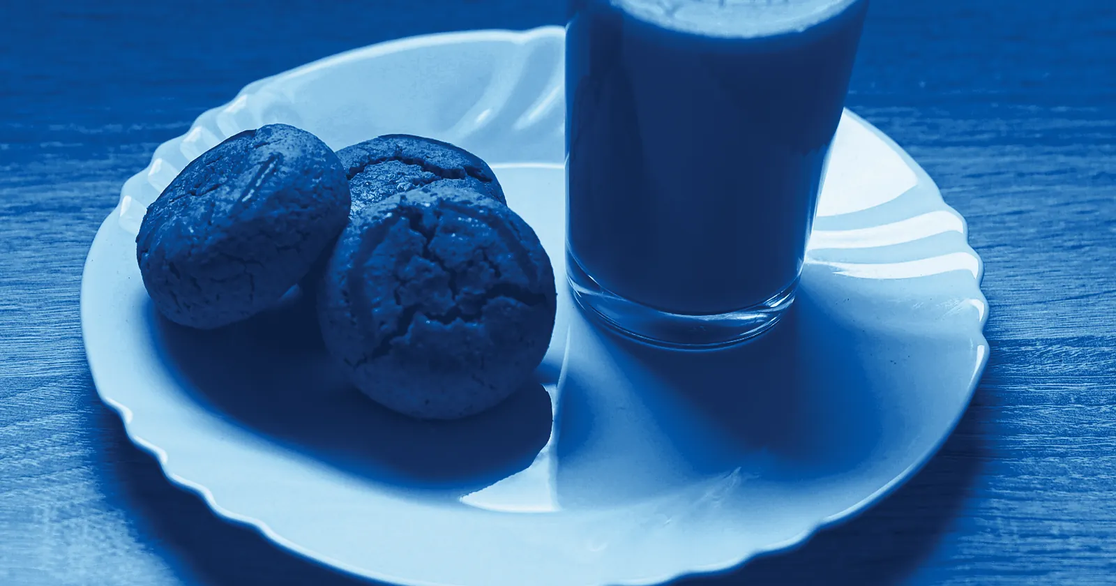 A glass of milky tea beside round biscuits on a white plate