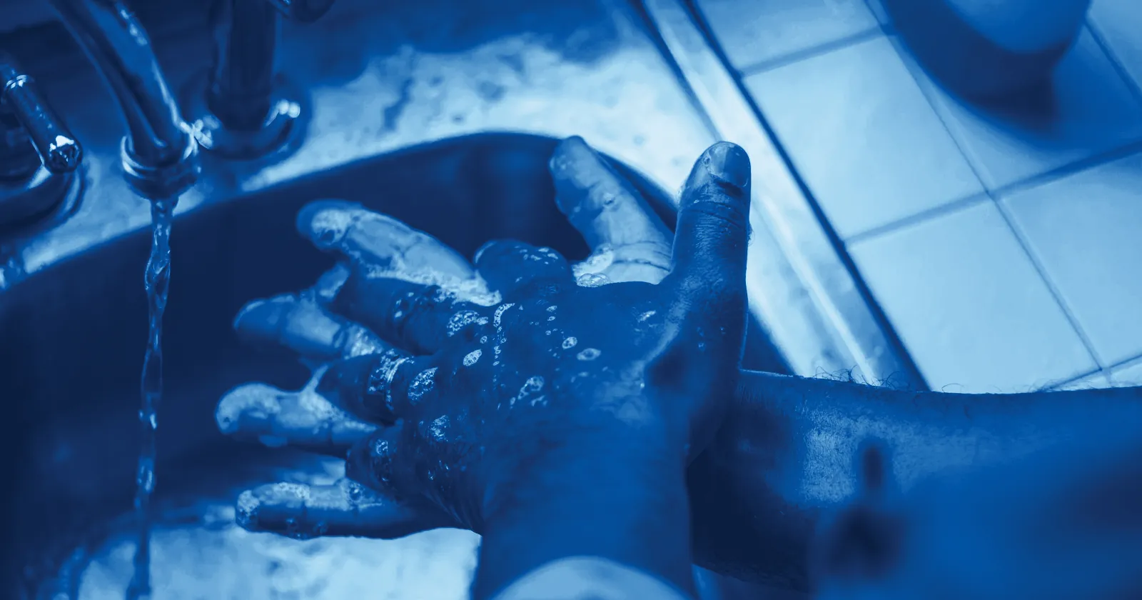 A person washing soapy hands under a running tap
