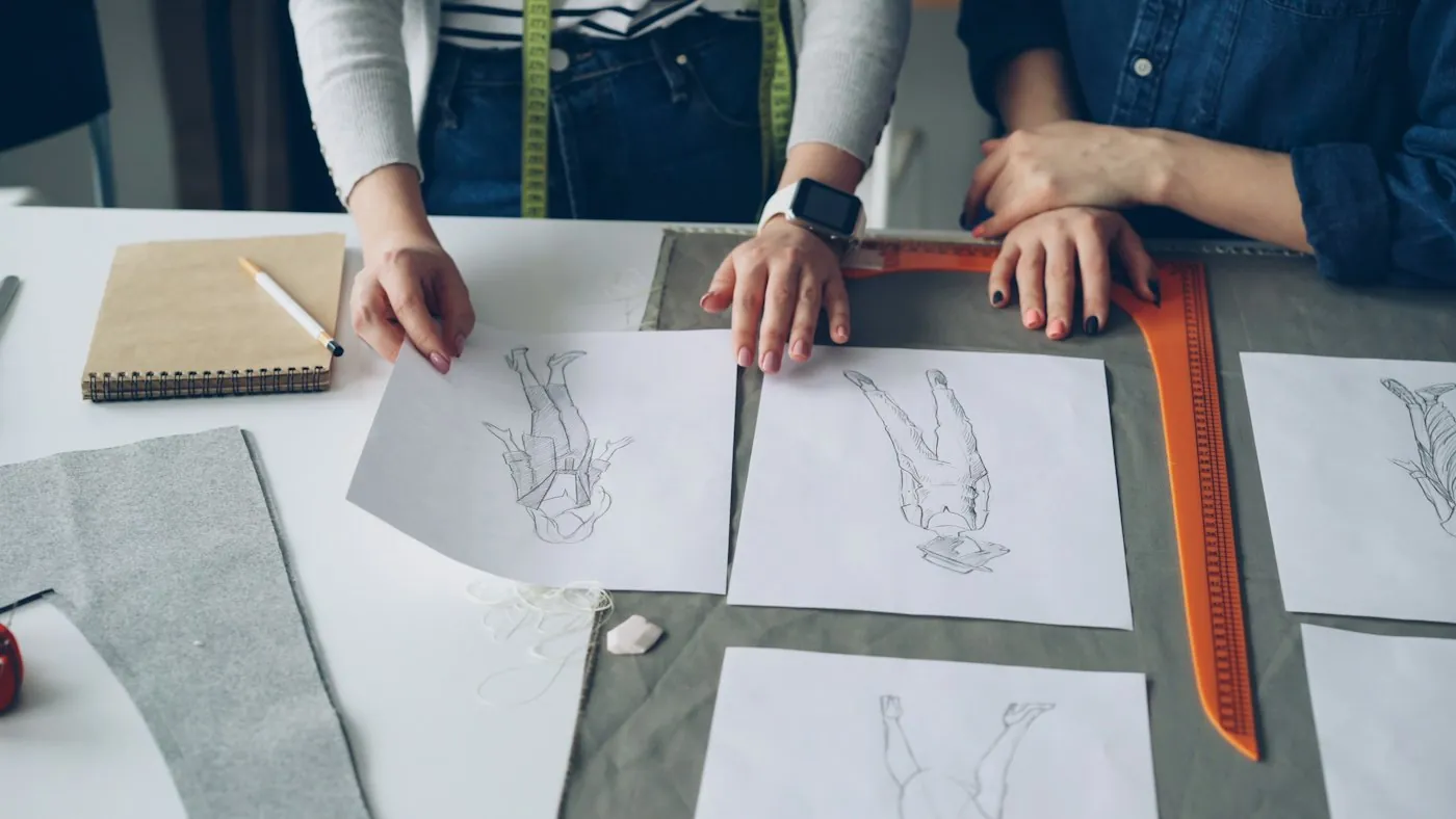 Designers comparing garment sketches laid out on a cutting table