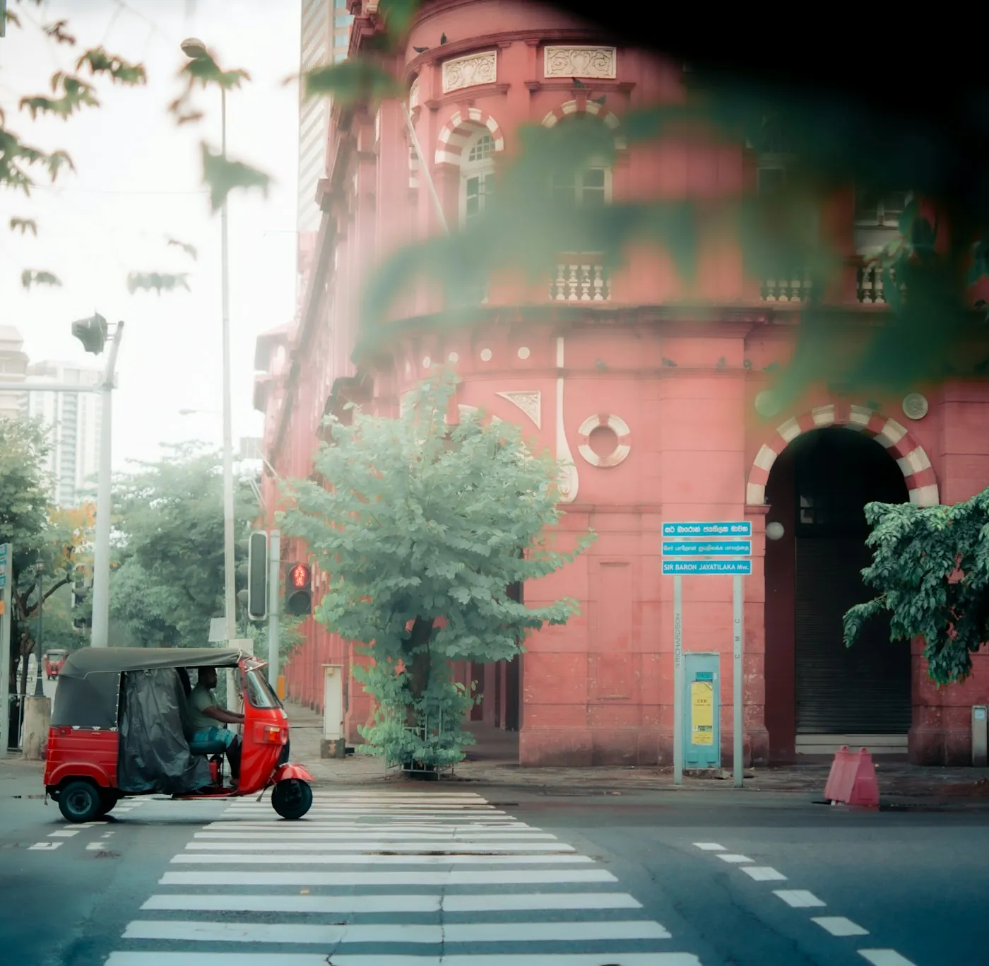 A red three-wheeler crossing a quiet junction in front of a colonial-era building in Colombo Fort